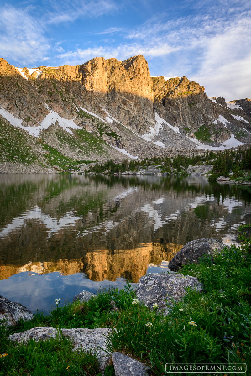 On a warm July morning a rugged unnamed peak near the northern border of Rocky Mountain National Park looks down on a still lake...